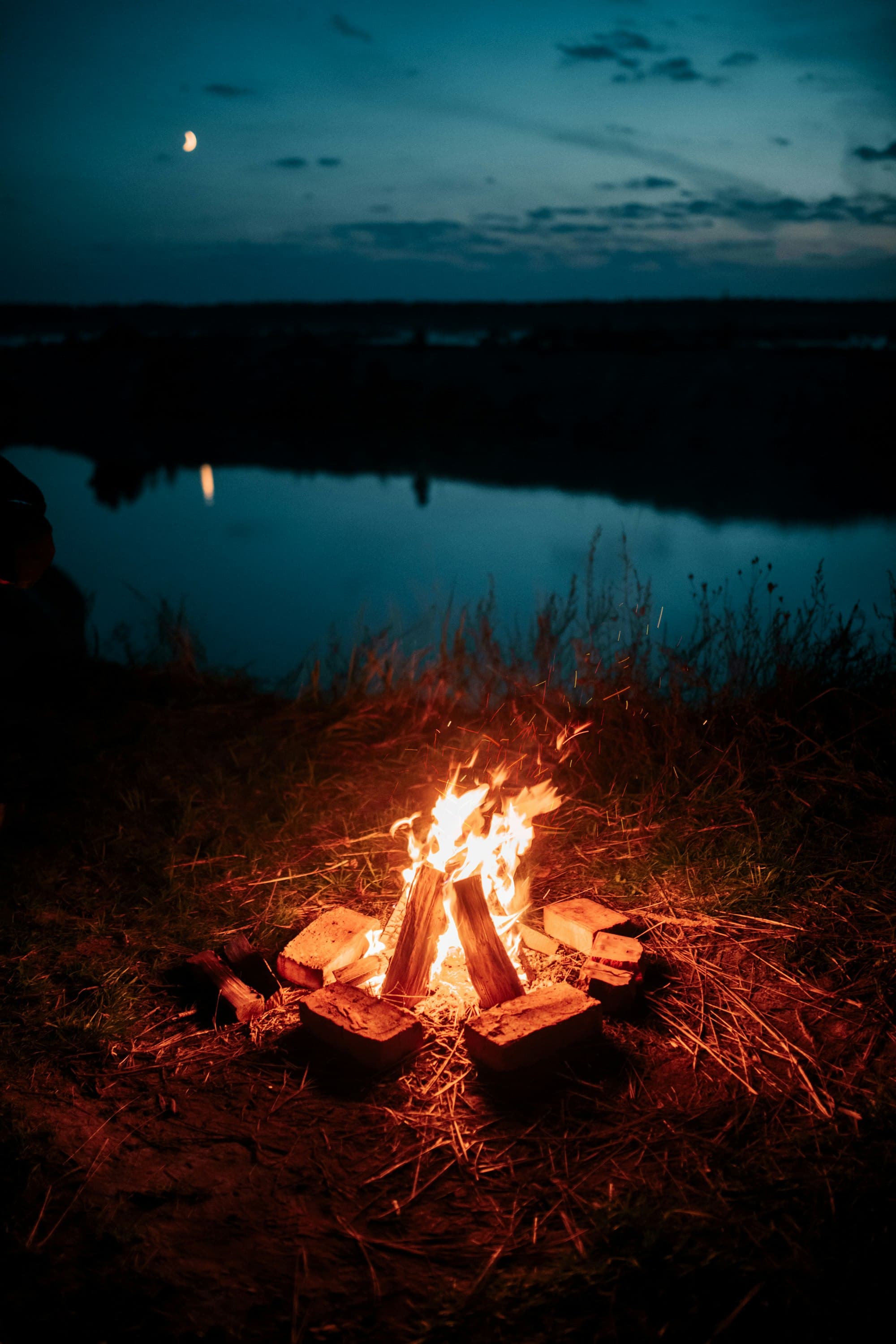 A bonfire glowing on a lake shore at dusk